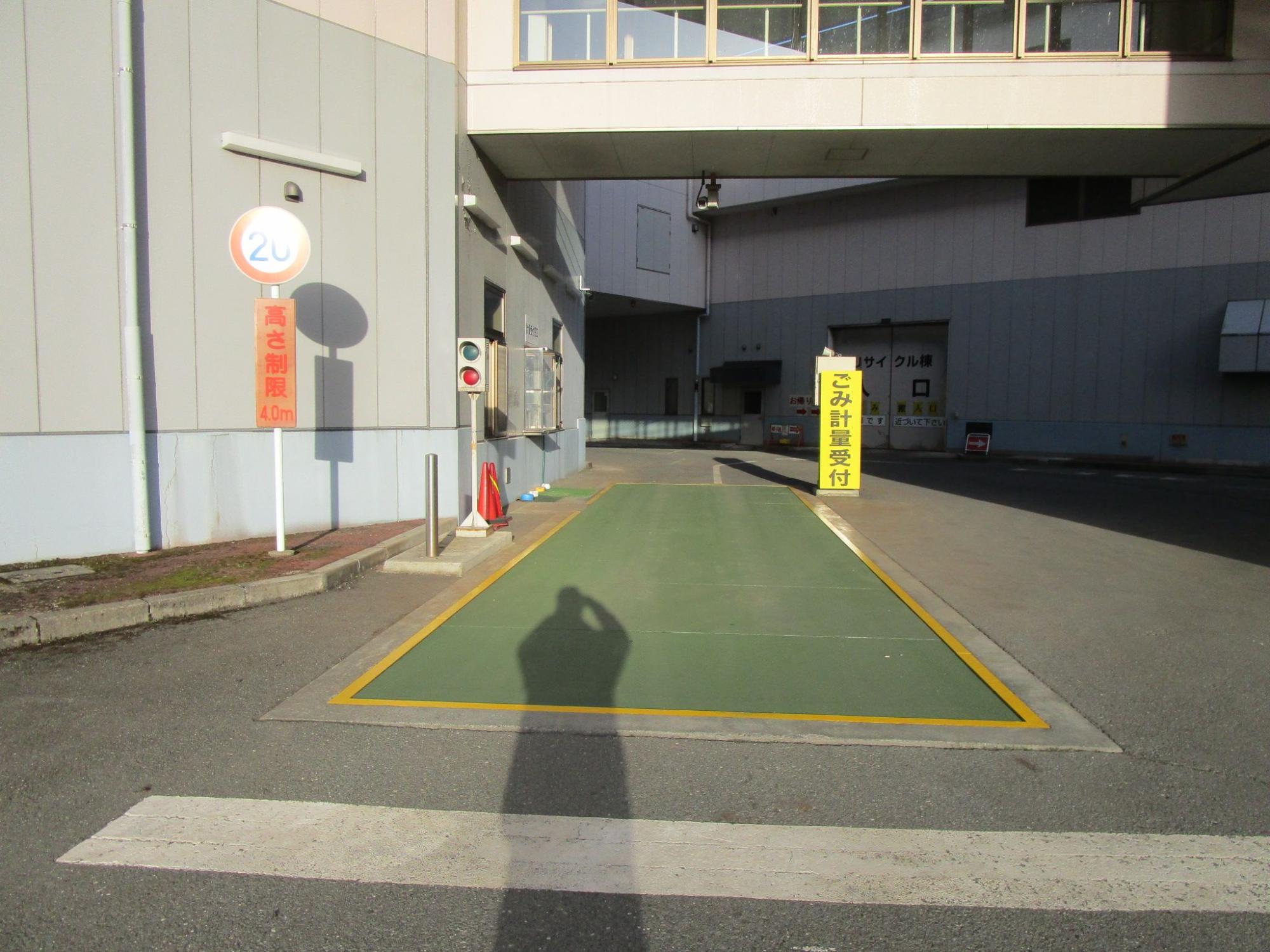 地面に設置された緑色の計量機に黄色い枠線が引かれ、「ごみ計量受付」と書かれた看板が立ててある計量機の写真