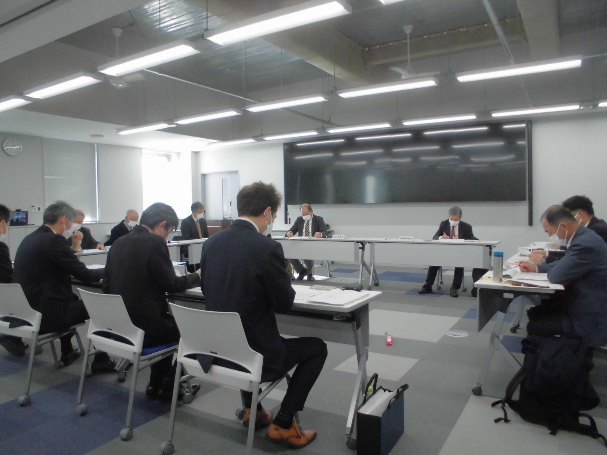 長机がロの字に設置された会議室内で関係者が座っている会議の様子の写真