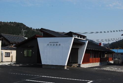 逆三角形のような形の白い壁に朽木診療所と書かれその奥に1階建ての建物が続く高島市民病院朽木診療所の写真