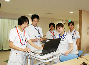 白衣を着た看護部の男女5名がパソコンをのぞき込んでいる様子の写真