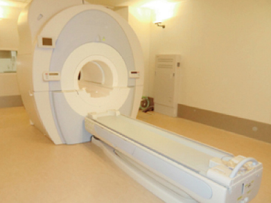 大きな機械の中央に体を通すための穴があり、手前に患者さんが寝るための台が置かれている装置の写真