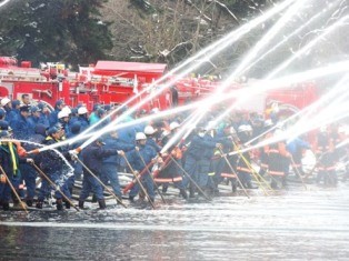 消防車の前に消防団員が並んで立ち全員で放水を行っている一斉放水の様子の写真
