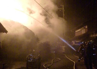 火の手が上がった建物に消防団員が放水を行っている様子の写真