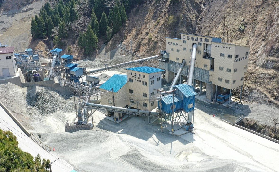 山の麓に高島鉱建株式会社と書かれた建物が建っている砕石現場を上空から撮影した写真