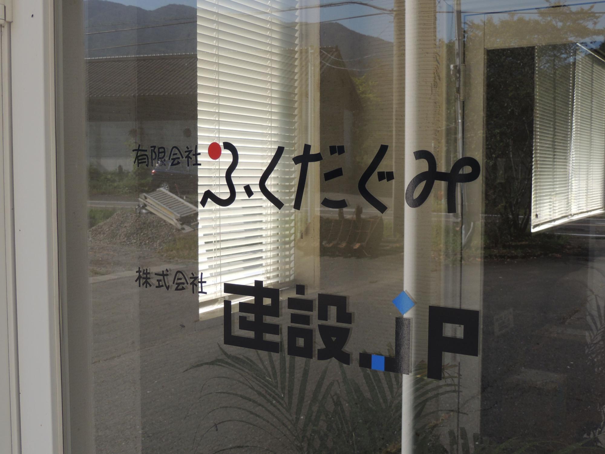 建物入口の窓ガラスに書かれた有限会社ふくだぐみ、株式会社建設JPの文字をアップで撮影した写真