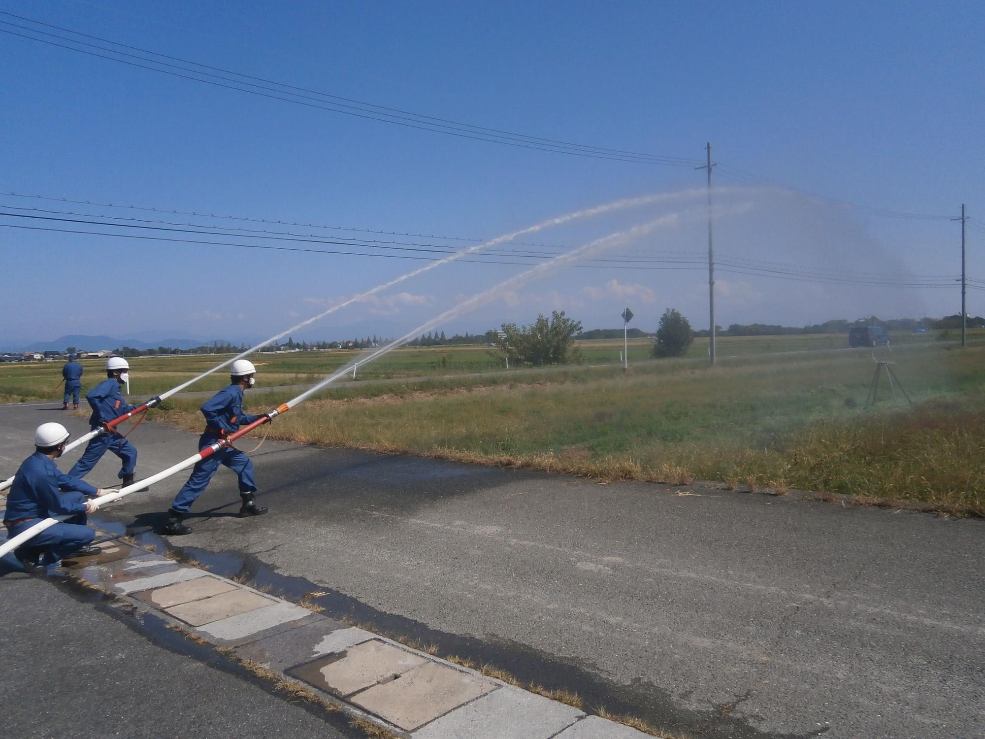 2名の消防団員が畑に設置された的に向かって放水を行っている様子の写真