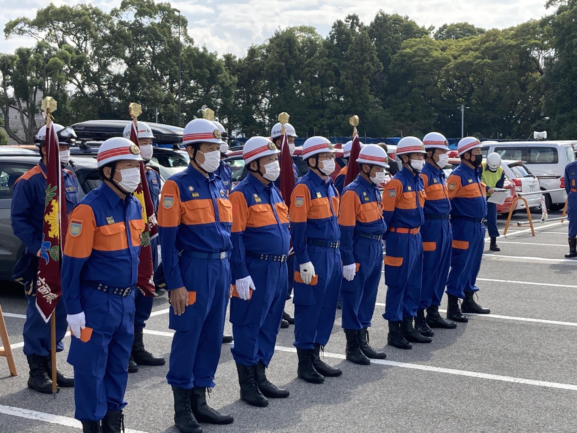 後列に旗を持っている団員の前に8名の滋賀県消防協会役員の方々が並んで立っている写真