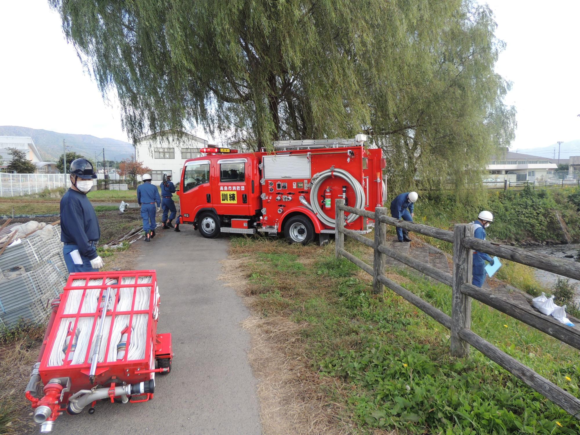 川沿いに停車した消防車の周りで準備をしている消防団員の写真
