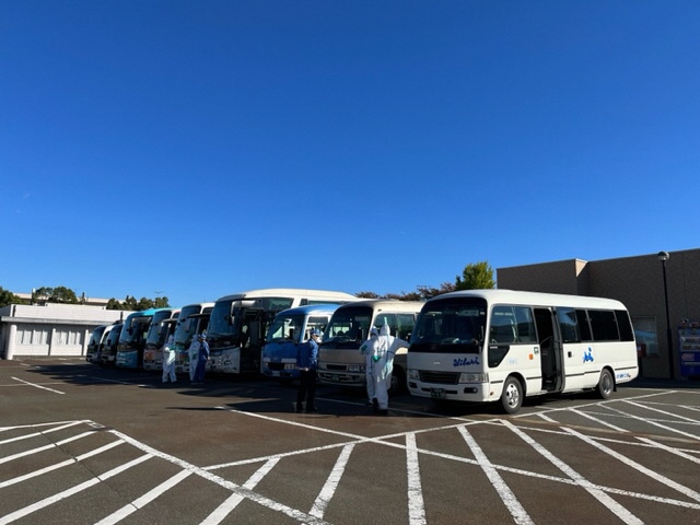 駐車場に9台の輸送用のバスが停車して並んでいる写真