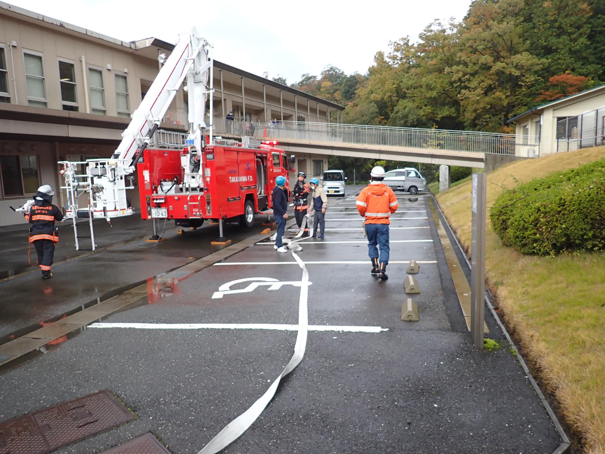 施設職員がホースを延長し消防車へ水を送る様子