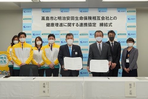左側に締結書を持った明治安田生命の高橋さんとその関係者4名、右側に締結書を持った福井市長とその関係者2名が立っている締結式の写真