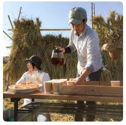 稲が干されている田んぼの中で、コーヒーやお茶菓子を準備している様子の写真