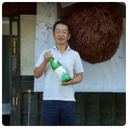 福井弥平商店の店先で日本酒の瓶をもつ福井社長の写真