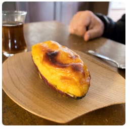 木のお皿の上に乗せられた、サツマイモの皮がそのまま器として使われているスイートポテトの写真