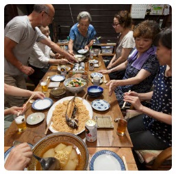 食卓に鯖寿司や鯖そうめんなどの料理が並べられ、皆で座って食べようとしている様子の写真