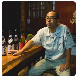 日本酒の瓶が並ぶカウンターに腰掛け、話をする上原社長の写真
