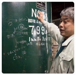 深緑色の大きなタンクにチョークで書いて説明をする吉田さんの写真