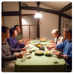 たくさんの料理が並んだ食卓に、右側に前川さんご夫婦、左側に中嶋さんら3人が座り、笑顔で食事を楽しんでいる様子の写真
