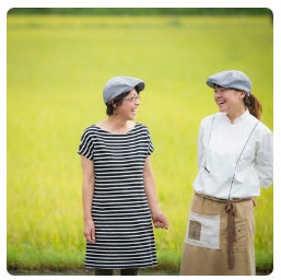 田園風景を背景に、向かい合って笑っている鈴木和枝さん、静香さん親子の写真
