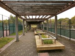 テニスコートのフェンスとフェンスの間に木製のベンチが設置された写真