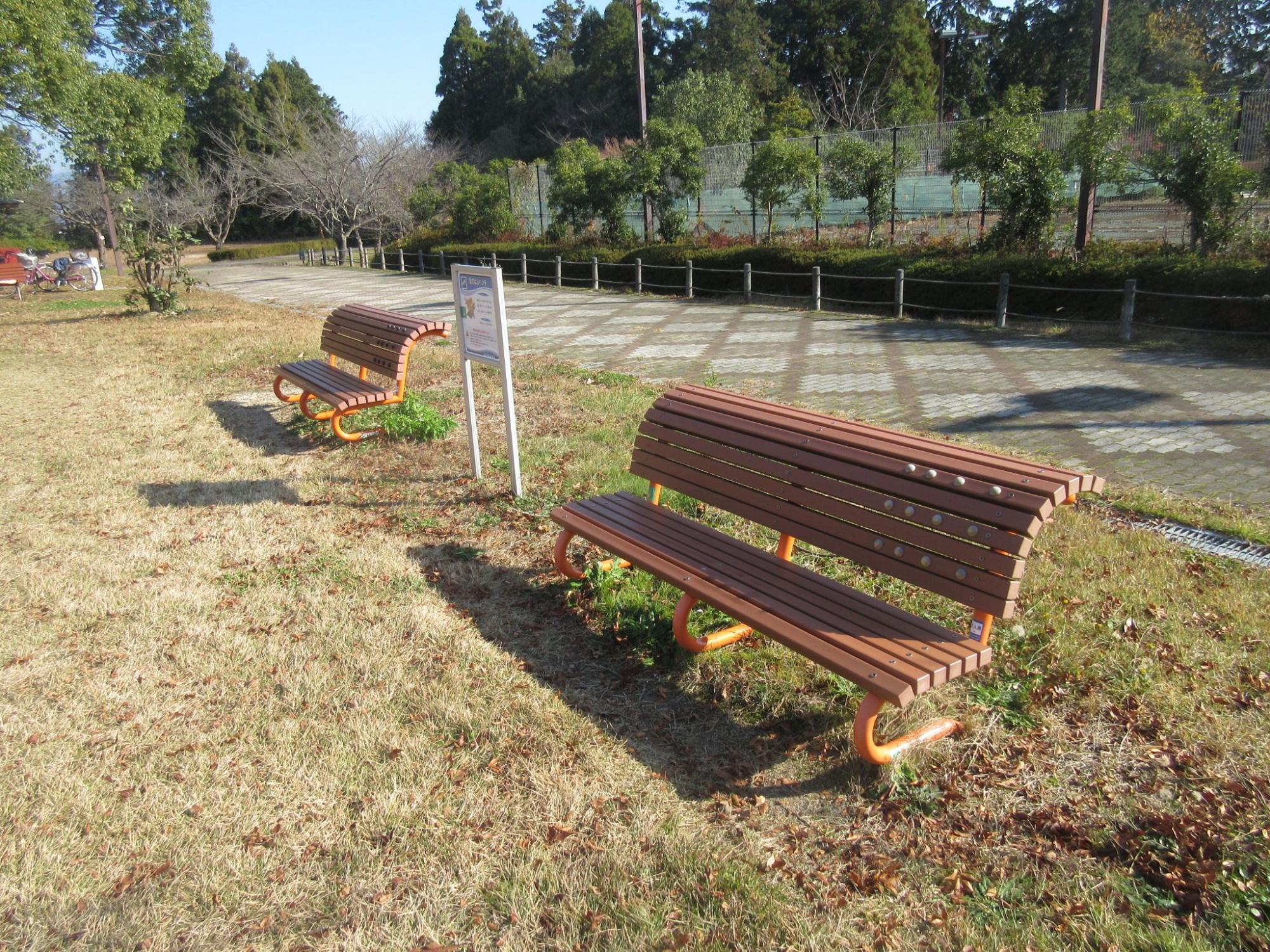枯れた芝生の広がる公園内に設置されたベンチの写真