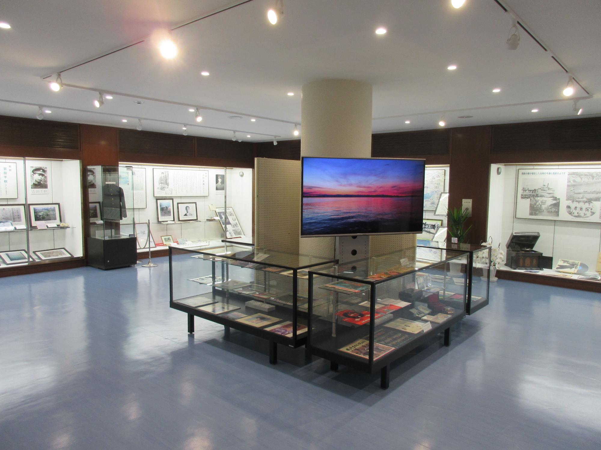 中央にスクリーンがありガラスケースに展示品が展示された展示ホールの写真