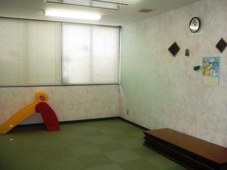 部屋の端に長机が畳んで重ねて置いてあり、幼児用の滑り台がある多目的ルームの写真