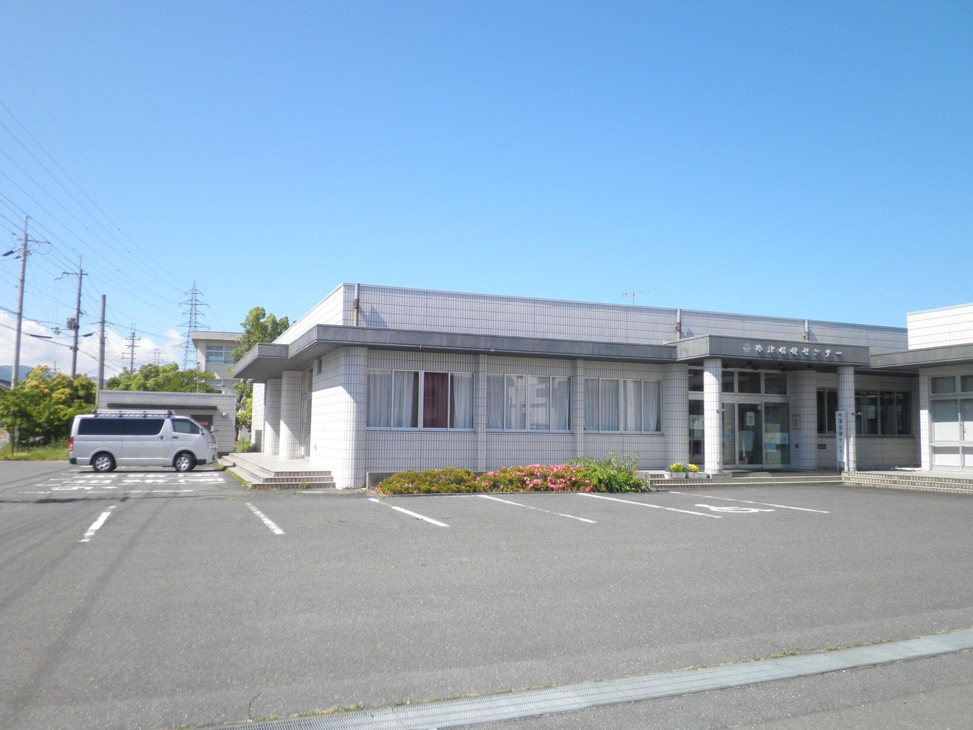 白とグレーを基調とした建物で、左側と正面に広々とした駐車スペースがある今津保健センターの外観写真