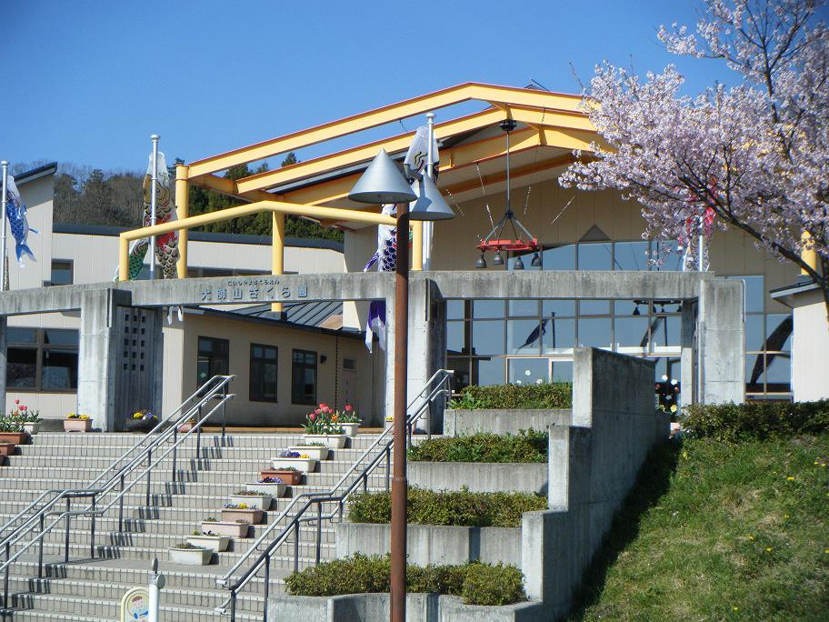 入口に続く階段に花が植えられたプランターが飾られ、建物の右側にに綺麗な桜が咲いている大師山さくら園の外観写真