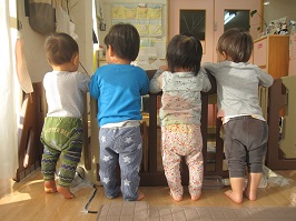 横に並び、つかまり立ちする4人の0歳児さんの後ろ姿の写真