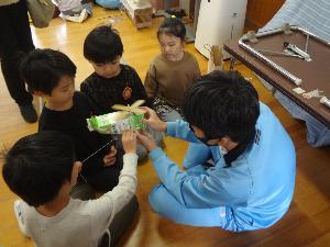 一人の中学生の周りに集まり、竹トンボを見せてもらっている子どもたち