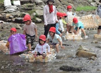 ペットボトルで作った筏に乗って川遊びをしているこどもたち