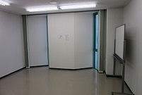 部屋に対して斜めに2つ窓がついており、右側の壁際にホワイトボードが置かれている会議室2－Bの写真