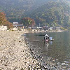 砂浜と湖の境界線が続く奥に集落や山々が見える写真