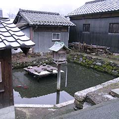 住宅が並ぶ中にある、石垣に囲まれたため池の写真