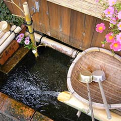 柄杓などが置かれている竹筒から水が流れ込む水路の写真