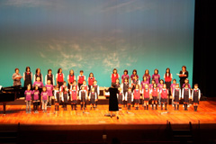 指揮に合わせて歌を歌っている小学生の合唱団の写真