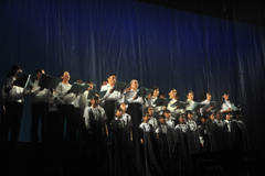 ステージに3列に並んで立っている人達が歌っている合唱の様子を左下から撮影した写真