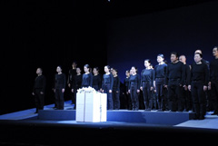 ステージに全身黒色の服を着た人たちが立っている前に白色の大きな箱が置かれている写真