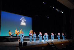 後方で黄色の法被姿の人たちの演奏に合わせて前方で水色の着物を着た人たちが踊っている様子の写真