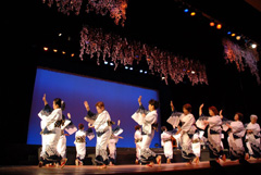 裾や袖に黒色の柄が入った白色の着物を着た女性たちが踊っている様子の写真