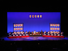 ステージ上に設置された3つの台の上に座った演者たちが笛や鼓などの楽器で演奏を行っている写真