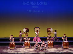 7つの大きな太鼓と前列で2つの小さな太鼓を叩いている演奏の様子の写真