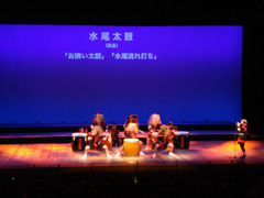 黒と赤色の衣装を着た6名の演者が太鼓の演奏を行っている様子の写真