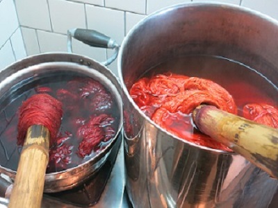 火にかけた大小の鍋に入れた布が赤色やオレンジ色に染まっている写真