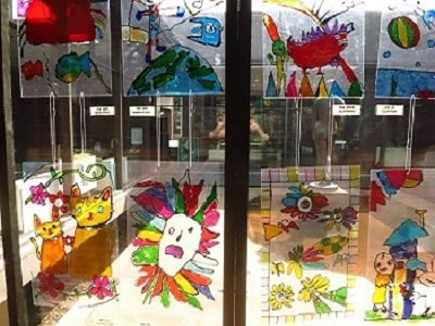 窓ガラスに子供たちが透明の板に描いた釣りをしたり大好きな猫などの作品が貼られている写真