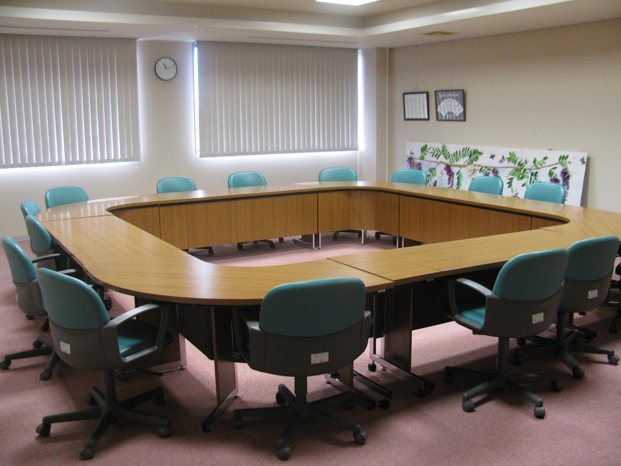 ロの字に配置された机に緑色の椅子が設置された会議室の写真