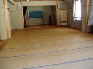 畳が敷かれた広々とした部屋で、前方に舞台と移動式の黒板がある2階会議室の写真