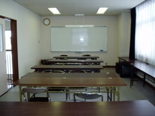 前方にホワイトボードと時計が設置してあり、長机が横に並びパイプ椅子が置かれた研修室の写真