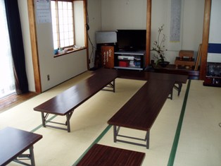 畳が敷かれた和室に高さの低い長机が並び、前方に盆栽や囲碁盤が置かれている会議室の写真